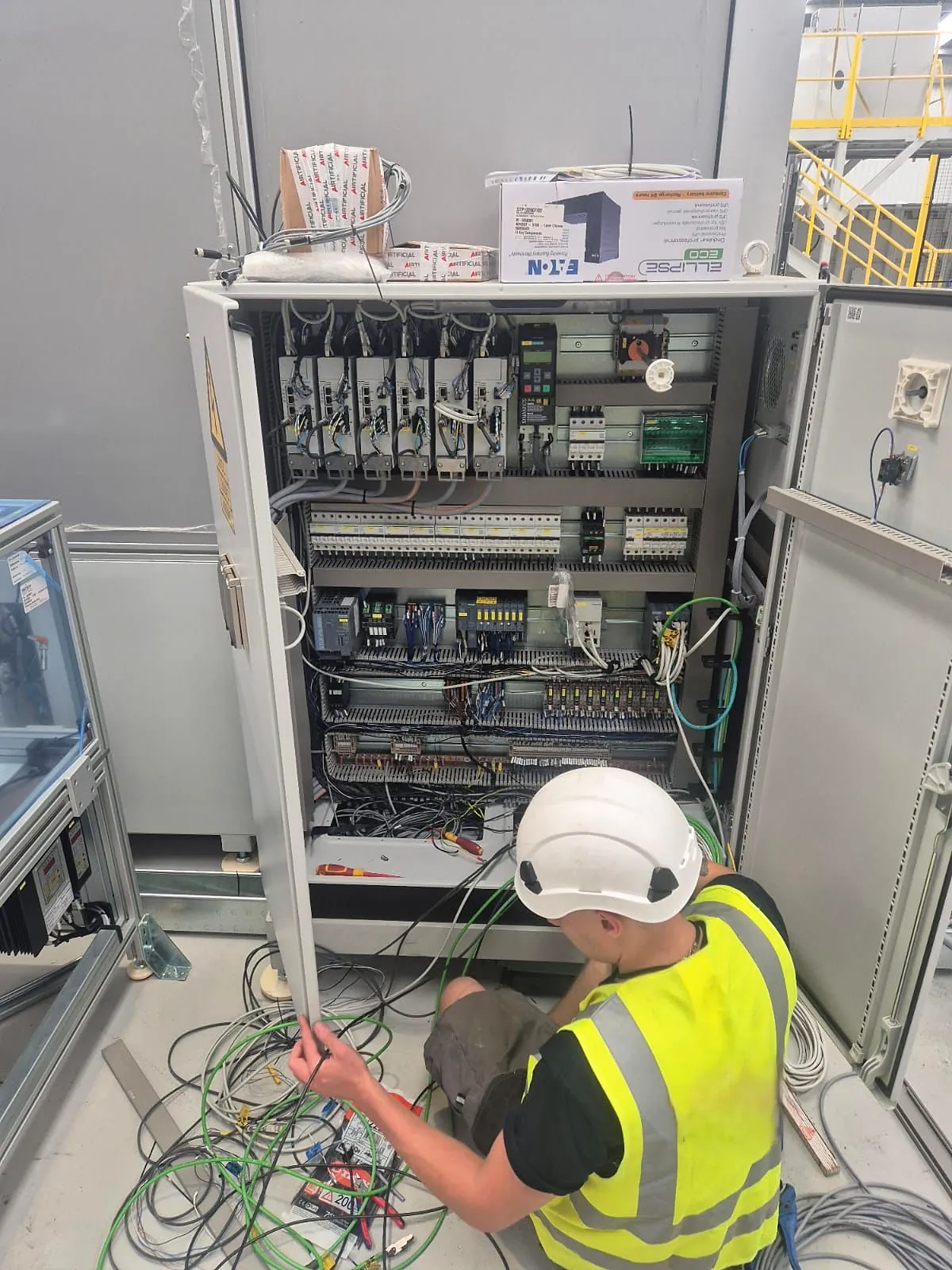 BMJB electrician wiring a control cabinet, seen from behind